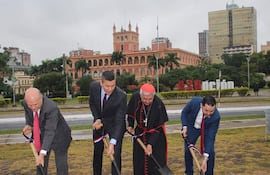 Santiago Peña Santi y otros tres hombres con palas en ceremonia exterior, ante un edificio gubernamental y banderas ondeando.