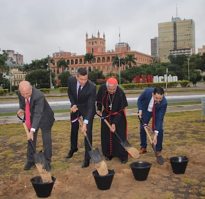 Santiago Peña Santi y otros tres hombres con palas en ceremonia exterior, ante un edificio gubernamental y banderas ondeando.