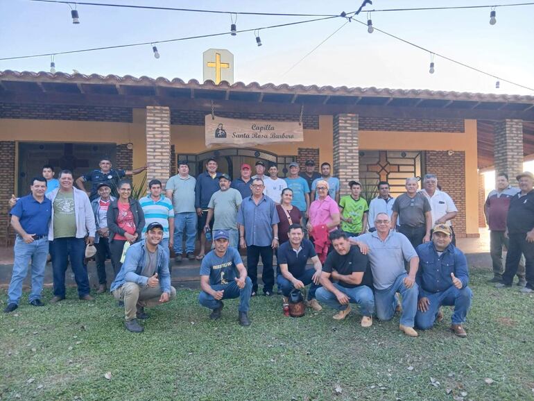 Grupo de personas sonrientes organizados en filas frente a la capilla, con un ambiente relajado y cielo claro.