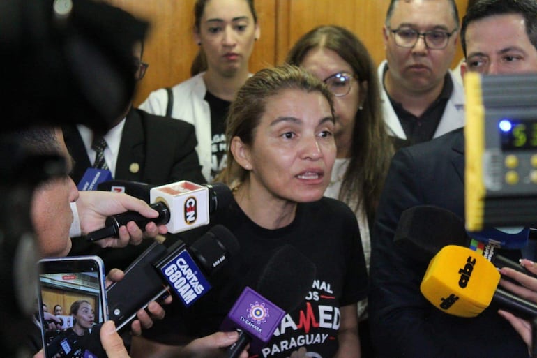 Mujer en camiseta negra con 'PARAGUAY' habla ante múltiples periodistas con micrófonos visiblemente presentes.