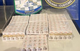 Paquetes apilados que parecen contener productos prohibidos, con escudos del Ministerio de Justicia y Aduana al fondo.