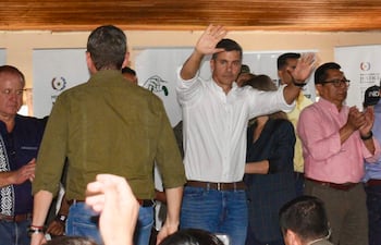 Santiago Peña en camisa blanca, levantando la mano mientras varios asistentes aplauden en un evento formal.