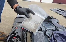 Persona con guantes sosteniendo un paquete dentro de un entorno exterior, rodeada de varios paquetes negros en el suelo.
