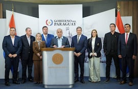 Núñez en chaqueta gris dirige la conferencia, rodeado por siete hombres y una mujer, todos en trajes formales, en un ambiente oficial.