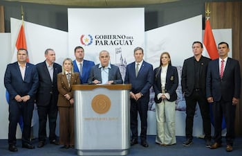 Núñez en chaqueta gris dirige la conferencia, rodeado por siete hombres y una mujer, todos en trajes formales, en un ambiente oficial.