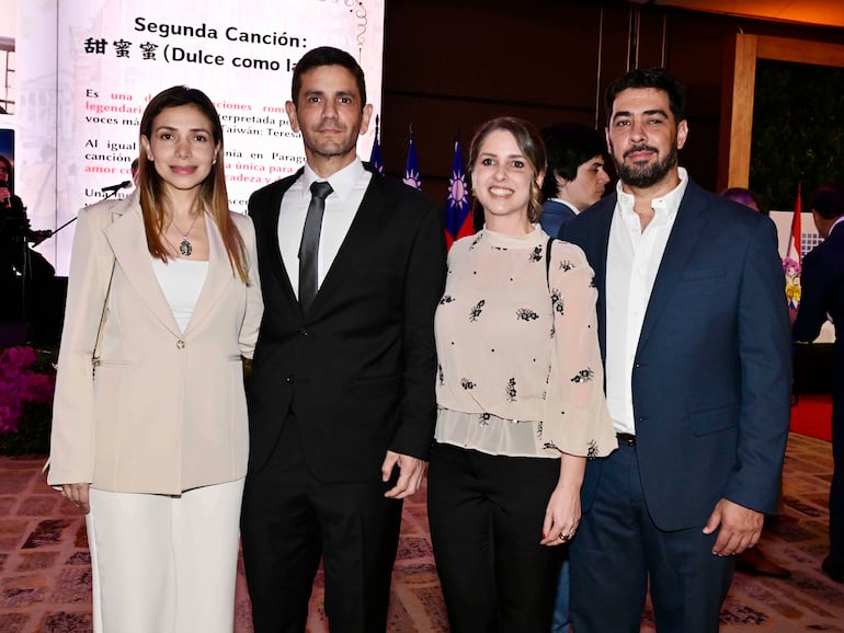 Cuatro asistentes sonriendo en ambiente formal; una mujer con traje claro, un hombre en traje oscuro, otra mujer con blusa floral, y un hombre con barba en camisa clara.