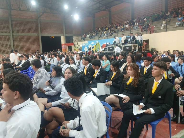 Grupo de jóvenes en camisas blancas y corbatas amarillas, atentos en evento con ambiente ceremonial.