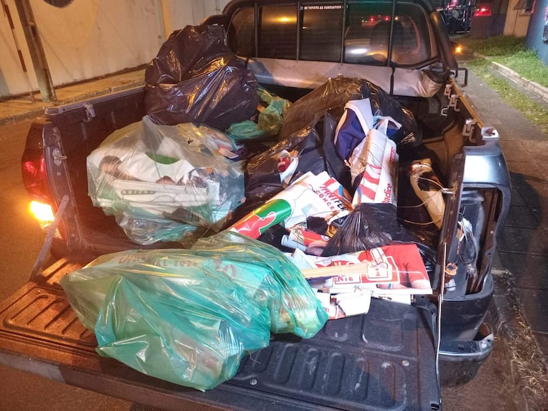 Camioneta cargada de bolsas de basura y carteles, en una calle de Asunción, ambientada de noche con luces cercanas.