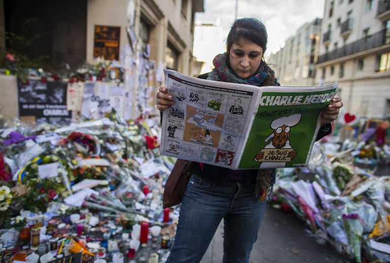 Una mujer leyendo un ejemplar de Charlie Hebdo, en medio de flores, tras el ataque