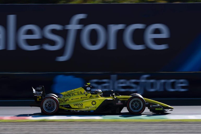 Automóvil de carreras en movimiento, amarillo y negro, con logos de Invicta y Lhg Mining en un circuito.
