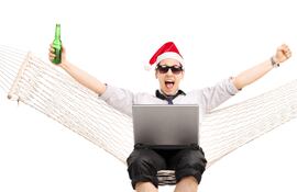 Un hombre con una gorra de papa noel en una hamaca paraguaya con una cerveza en la mano y una botella de cerveza