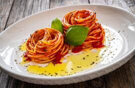 Un plato blanco con dos nidos de fideos cubiertos son salsa de tomate y aceite de oliva