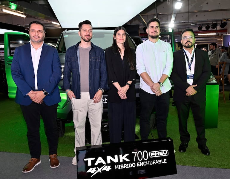 Cinco personas de pie en evento, incluido hombre con blazer azul y mujer con atuendo negro, frente al GWM TANK 700.