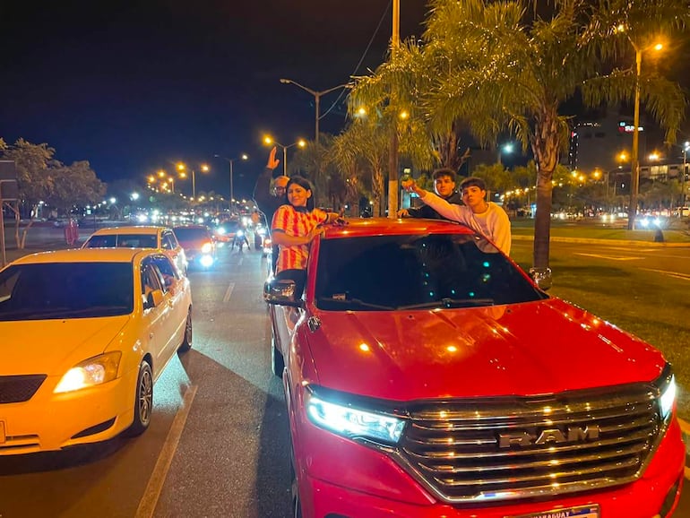 Cuatro personas sobre un vehículo rojo de marca RAM, con gestos festivos y alegría en una noche de celebración.