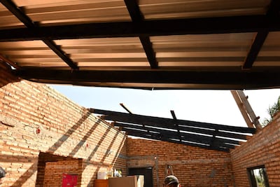 Persona con gorra en un interior dañado, con paredes de ladrillo expuesto y techo colapsado, mientras la luz del sol entra por arriba.