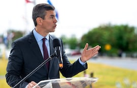Santiago Peña Santi en traje oscuro gesticulando frente a un atril, con banderas y un paisaje verde de fondo.