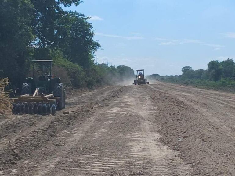 Dos tractores en un camino de tierra arando el terreno, rodeados de vegetación y un cielo parcialmente nublado.