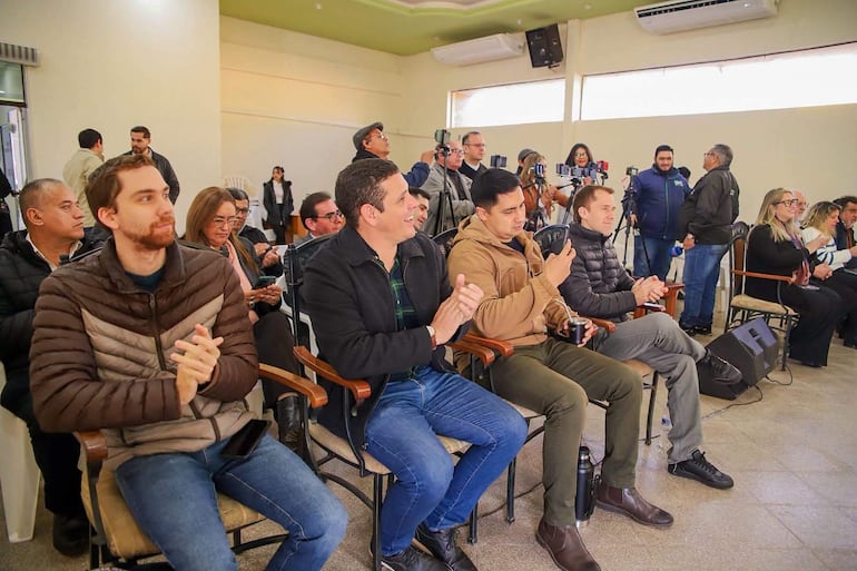 Asistentes aplauden en el evento de lanzamiento. Hombres con abrigos felices y atentos. Ambiente de sala de conferencias.