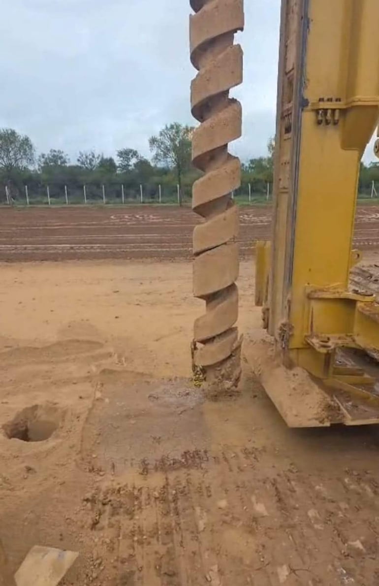 Primer plano de equipo de perforación en terreno húmedo, excavando para la fundación del hospital en un entorno despejado.