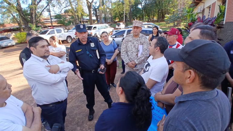 Oficial de policía gesticulando en conversación con ciudadanos, mientras una mujer y un hombre escuchan atentamente en un entorno abierto.