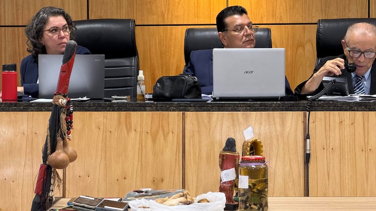 Tres personas en una reunión formal, un hombre canoso habla por teléfono mientras dos hombres escuchan atentamente.