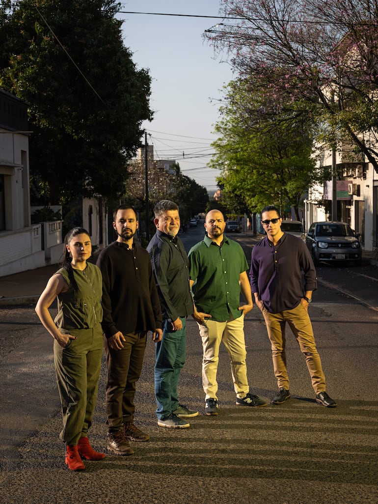 Cinco hombres y mujeres de pie en una calle al atardecer.