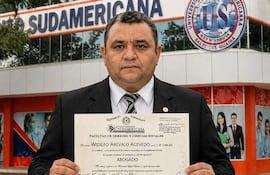 Hombre robusto en camisa clara y chaqueta oscura sosteniendo un diploma, mostrando orgullo en la Universidad Autónoma Sudamericana.