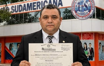 Hombre robusto en camisa clara y chaqueta oscura sosteniendo un diploma, mostrando orgullo en la Universidad Autónoma Sudamericana.