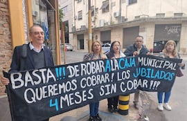 Hombre canoso en saco lidera la protesta junto a mujeres que sostienen un banner con demandas de jubilados en la calle.