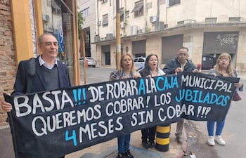 Hombre canoso en saco lidera la protesta junto a mujeres que sostienen un banner con demandas de jubilados en la calle.