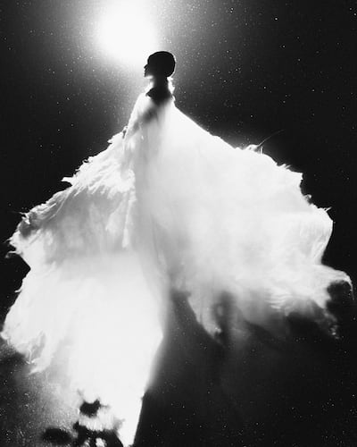 Silhouette de figura en vestido voluminoso, destacándose en fondo oscuro iluminado, creando un efecto dramático en escena artística.