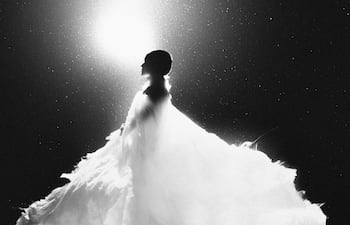 Silhouette de figura en vestido voluminoso, destacándose en fondo oscuro iluminado, creando un efecto dramático en escena artística.
