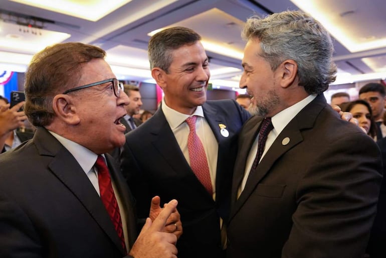 Santiago Peña en chaqueta gris sonríe mientras conversa con Mario Abdo Benítez y Pedro Alliana en un ambiente elegante.