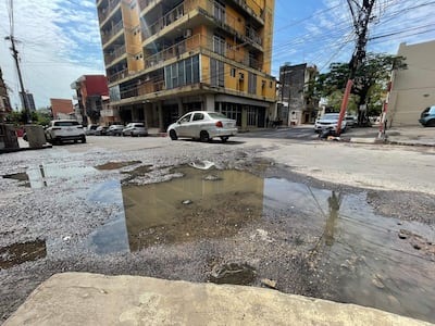 Escena urbana con un charco en la calle, edificios amarillos y vehículos estacionados en un ambiente deteriorado.