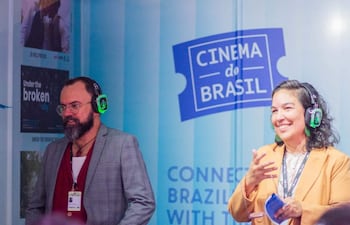 Mujer con chaqueta amarilla habla sonriente, mientras hombre de saco gris escucha atentamente en evento de cine.