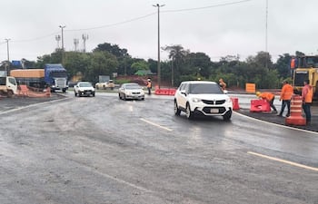 Trabajadores con chalecos naranjas y cascos amarillos dirigen el tráfico en carretera en construcción bajo un cielo nublado.
