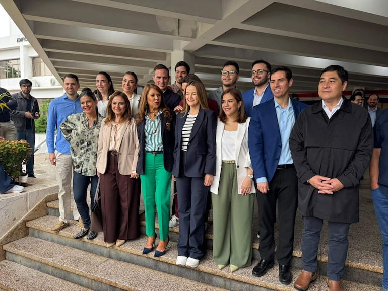 Sole Núñez y su equipo posan sonrientes en escaleras, vistiendo trajes formales en tonos variados.