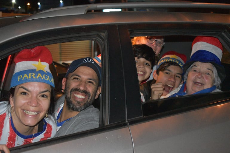Grupo de seis personas sonrientes en un automóvil, luciendo gorras y camisetas con colores nacionales de Paraguay, en un ambiente festivo nocturno.