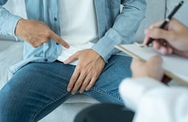 Hombre en el consultorio médico señala hacia sus genitales.