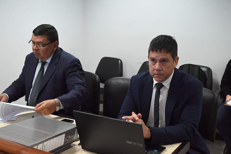 Javier Silvera, vestido con traje oscuro y corbata, revisa documentos frente a un portátil en ambiente formal.
