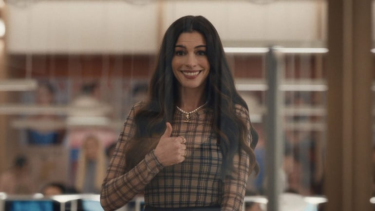 Mujer con sonrisa amplia y pulgar arriba, en ambiente de oficina con detalles de trabajo al fondo.