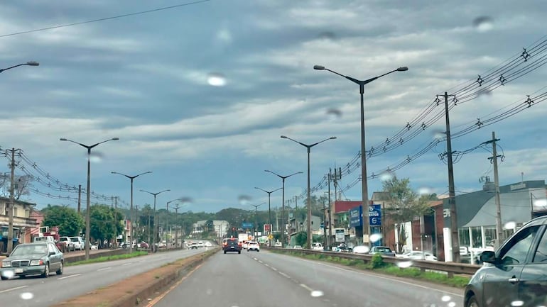 Carretera urbana en día nublado, con dos coches en movimiento y sin personas a la vista.
