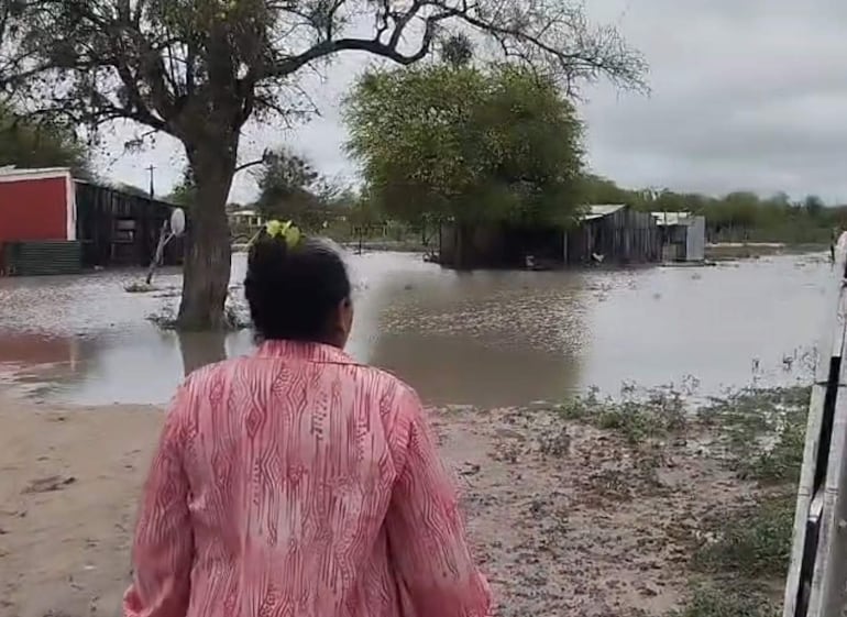 Mujer de espaldas con camisa rosa caminando en terreno inundado, rodeada de agua y casas semi-sumergidas.