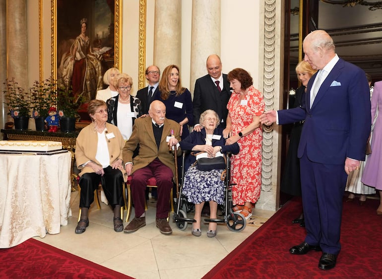 El rey Carlos III de Gran Bretaña saluda a los centenarios Joan Illingworth, John Jervois y Mary Wood mientras les entrega tarjetas de cumpleaños a las personas que cumplen cien años hoy, en una recepción en el Palacio de Buckingham, para celebrar el centenario del nacimiento de la reina Isabel II. (Jordan Pettitt / POOL / AFP)