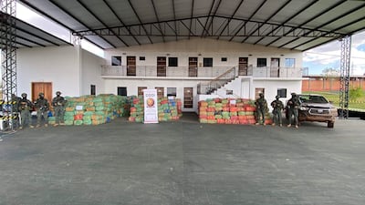 Seis soldados en uniforme militar con armas, alineados frente a paquetes de colores, con cartel de CODI en el centro.