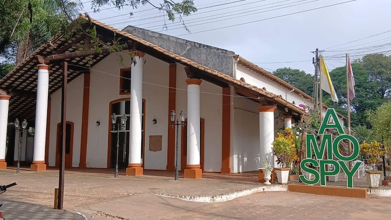 Edificio colonial con paredes blancas y detalles naranjas, sin personas visibles y vegetación alrededor.
