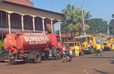 Camión rojo de 'BOMBEROS VOLUNTARIOS' en calle de Hernandarias, con vehículos amarillos y naranjas alineados.