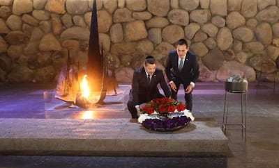 Rubén Ramírez Lezcano y Pedro Alliana en traje, colocando ofrenda circular con flores en ambiente ceremonial con fogata al fondo.