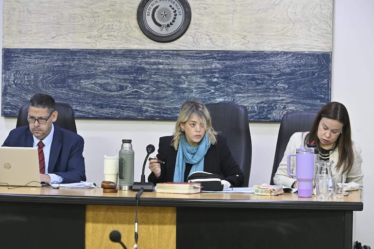 María Fernanda García, con abrigo negro y bufanda azul, habla mientras Juan Carlos Zárate y Yolanda Portillo la observan concentrados en documentos.