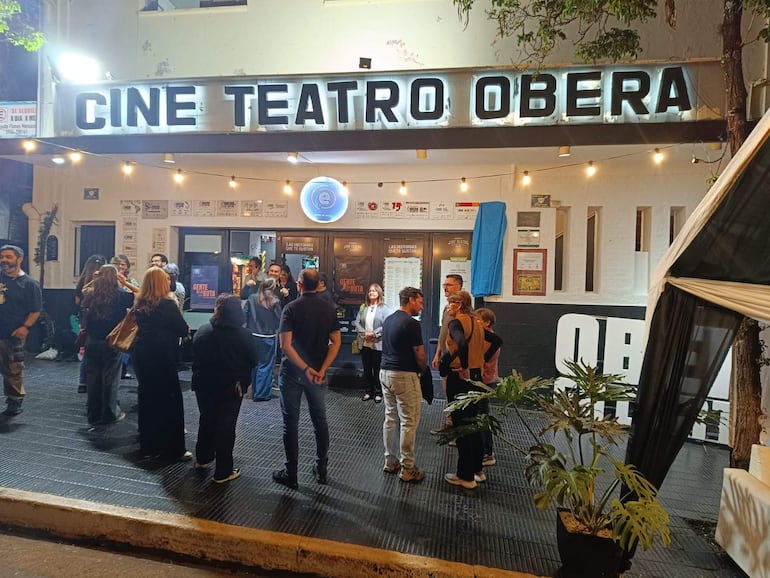 Grupo de personas conversando en la entrada del Cine Teatro Oberá, con expresiones alegres y diversa vestimenta.